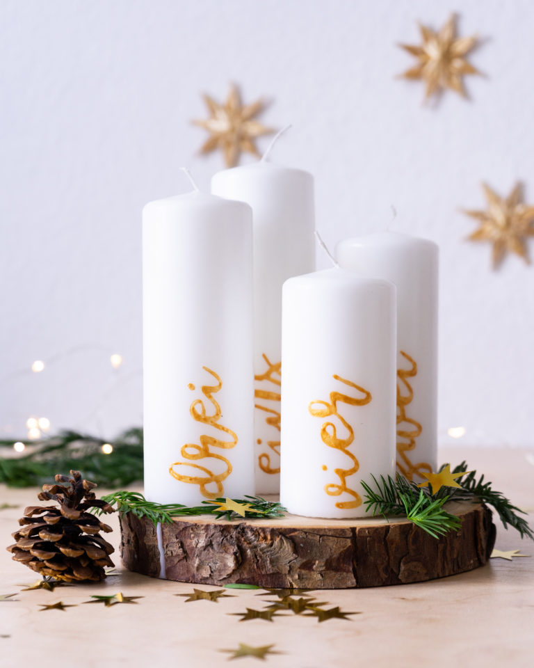 Adventi tömbgyertyák arany feliratokkal, ünnepi asztalon