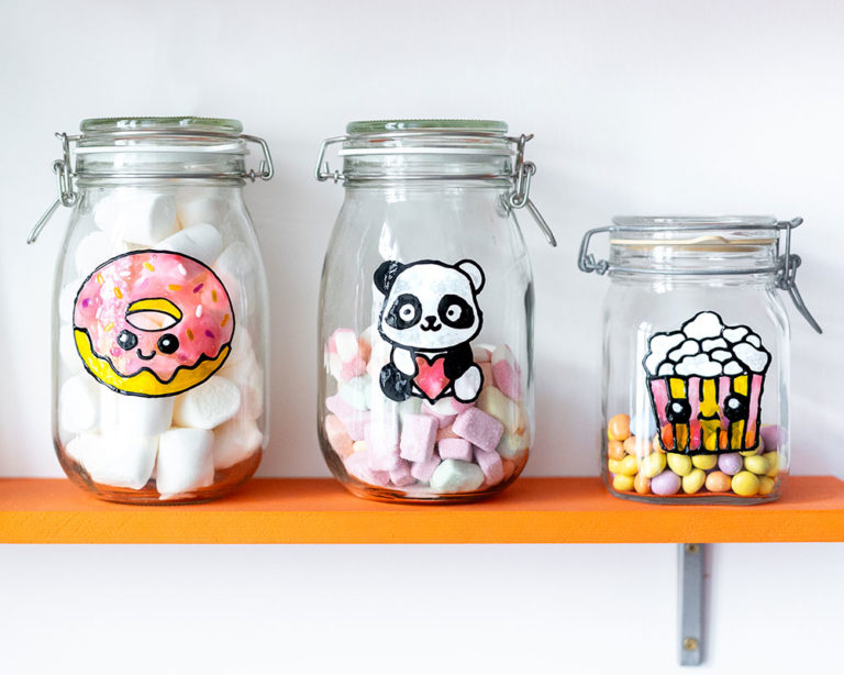 Három díszített befőttesüveg egy polcon: fánk, panda és popcorn